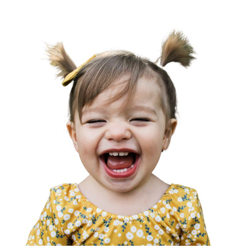 Young child with pigtails and a yellow floral top smiles widely, showing teeth, against a plain white background.